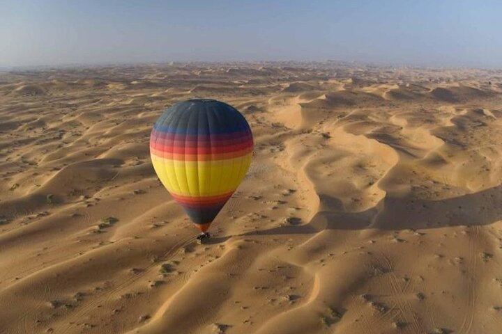 Experience the serene morning light as you float above endless desert dunes taking in stunning views of the oasis below and the warm glow of the sunrise in Dubai.
